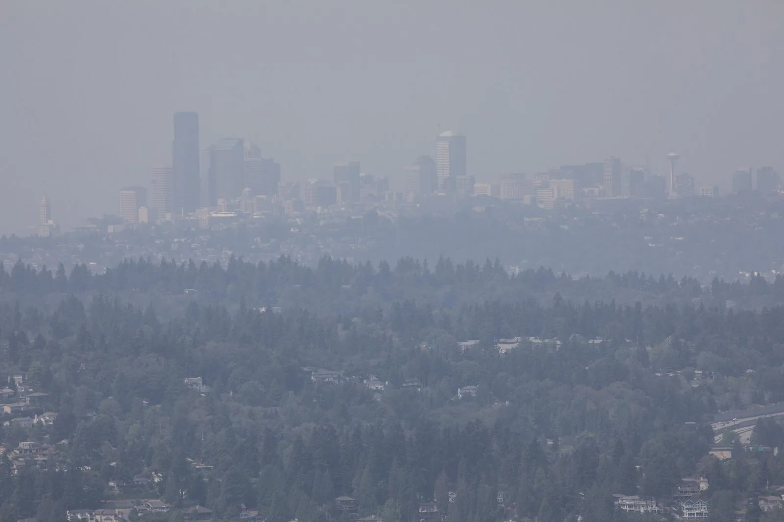 A wildfire-smoke haze obscures the Seattle skyline and evergreen forest as seen across the Puget Sound region