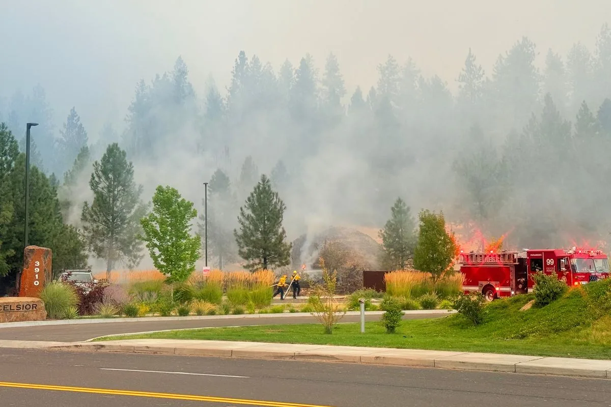 A fire truck and firefighters battle flames and heavy smoke near a residential street corner in Spokane, Washington during the Old Trails Fire