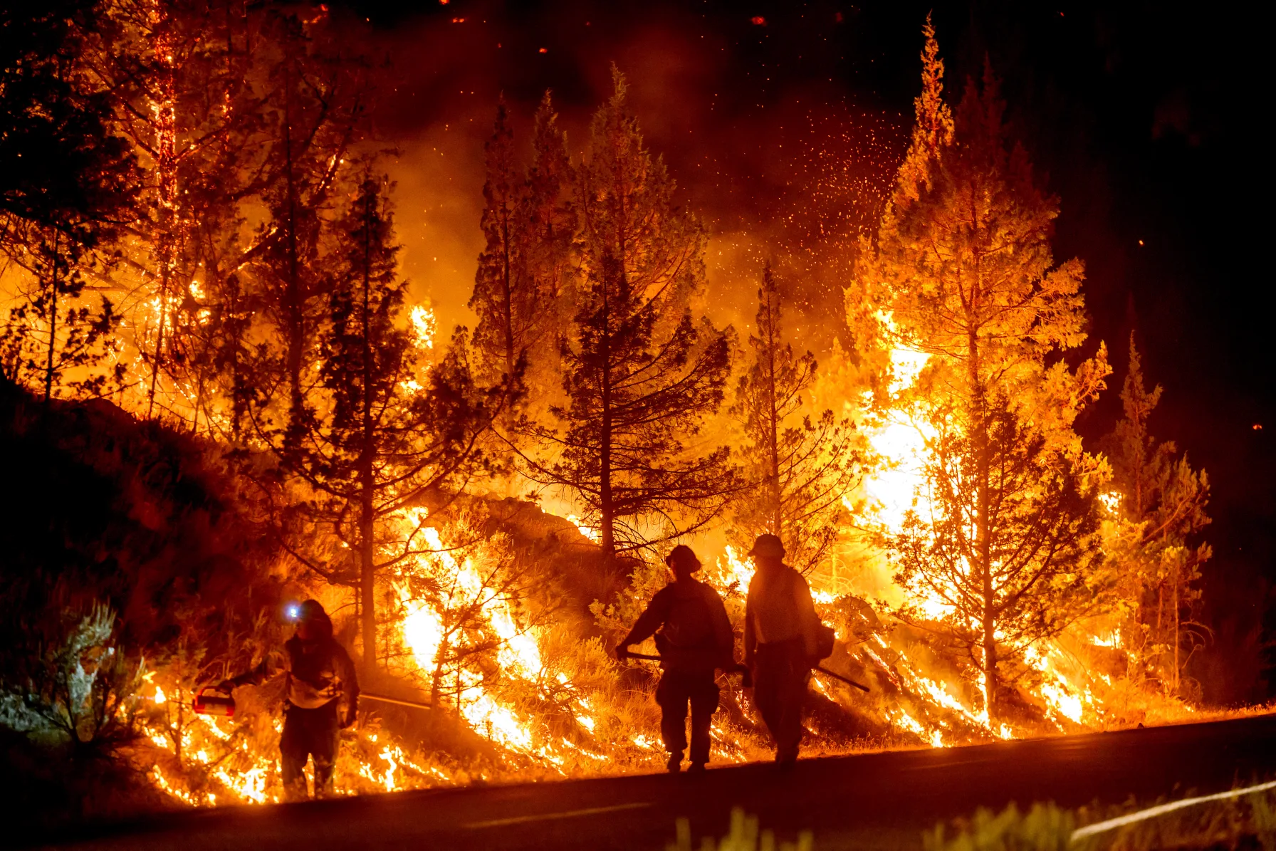Firefighters silhouetted against towering flames while battling the Bench Fire at night in Warm Springs, Oregon