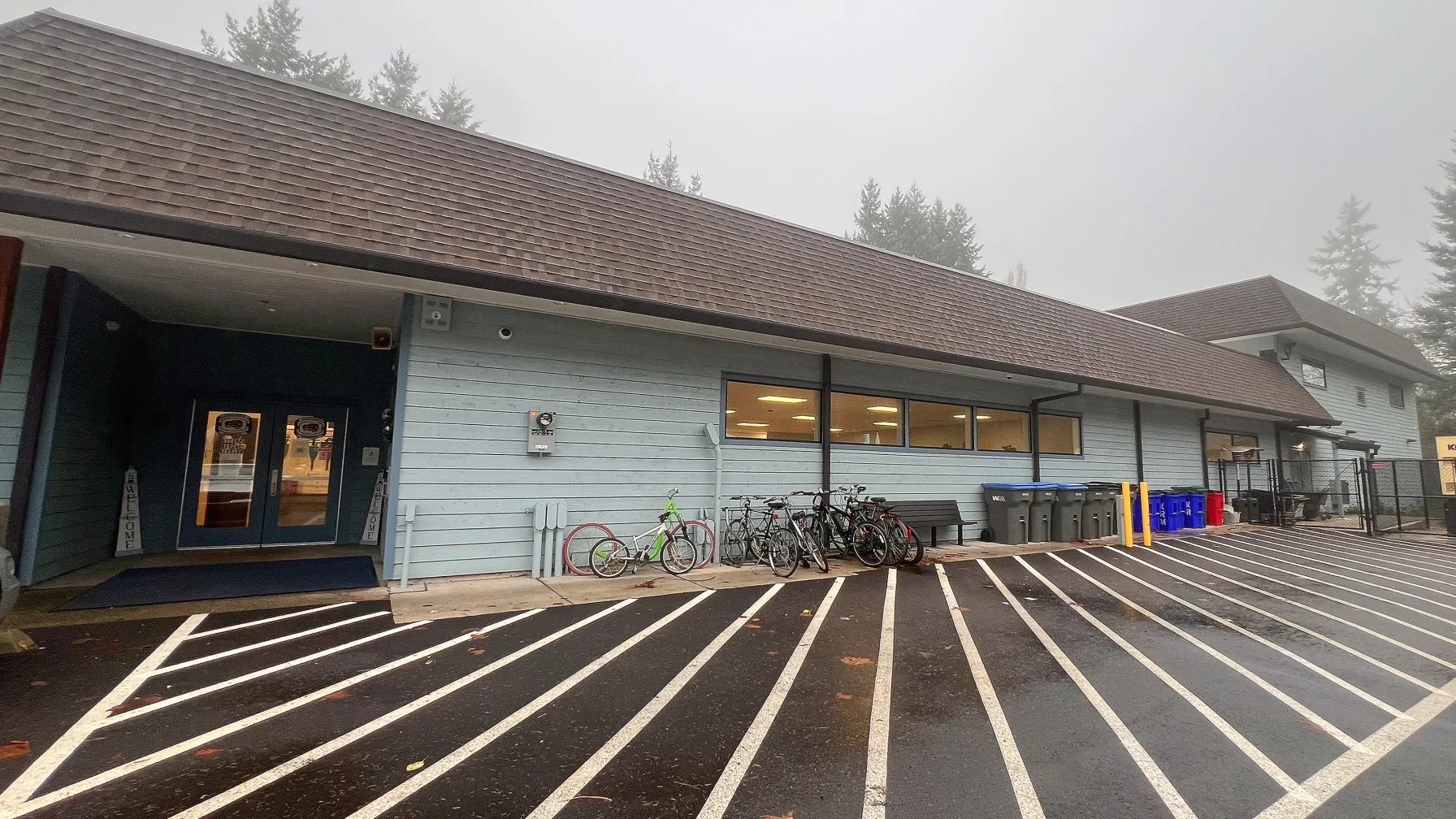 Exterior of the Pacific Building homeless shelter in Port Orchard, Washington, with bicycles parked near the entrance on a foggy morning