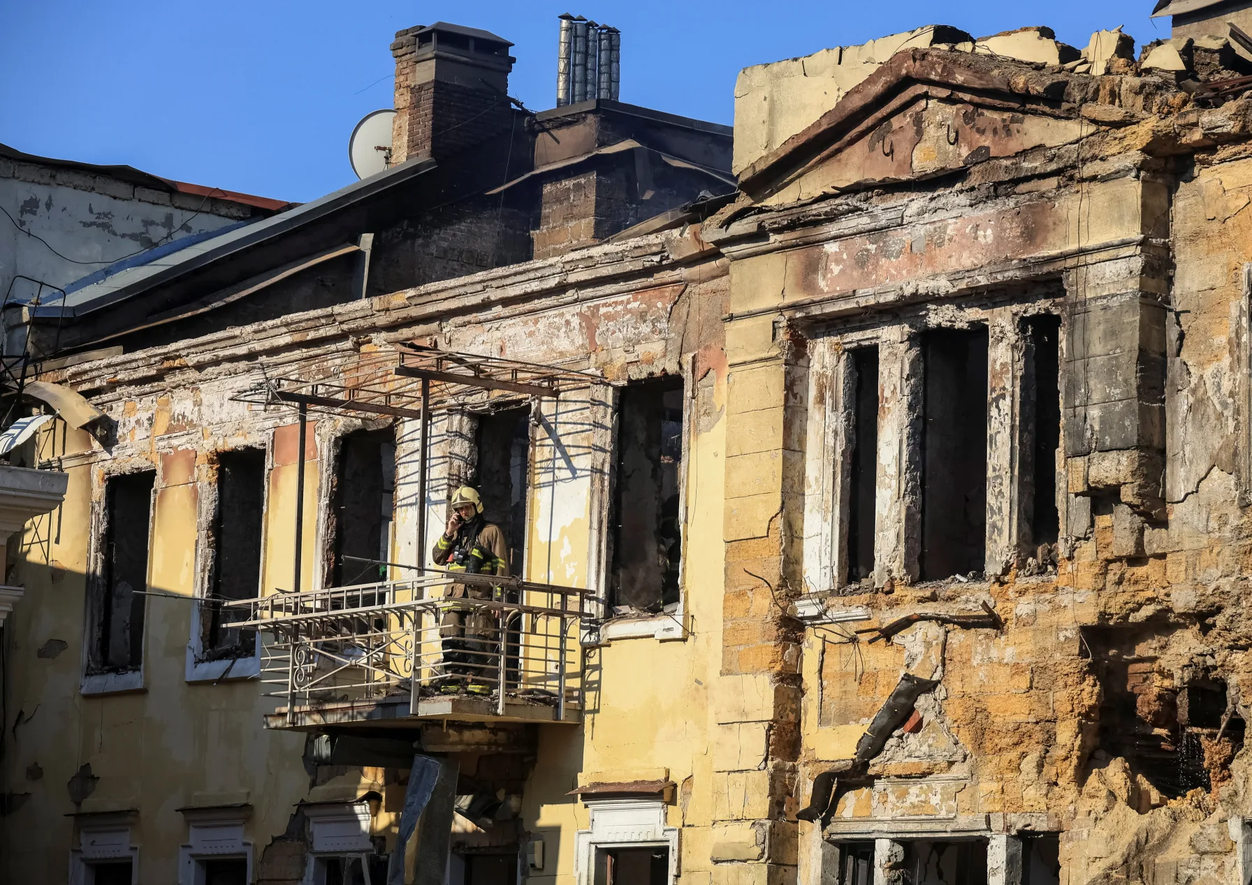 A firefighter stands on a damaged balcony inspecting a historic building with blown-out windows after a strike in Ukraine