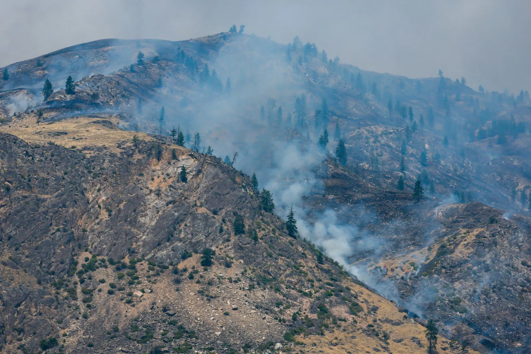 Smoke rises from the Kaiser Canyon fire burning across a scorched Eastern Washington ridgeline as firefighters work the line below
